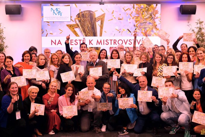 Velká skupina absolventů stojí na jevišti s certifikáty v rukou, v pozadí konfety