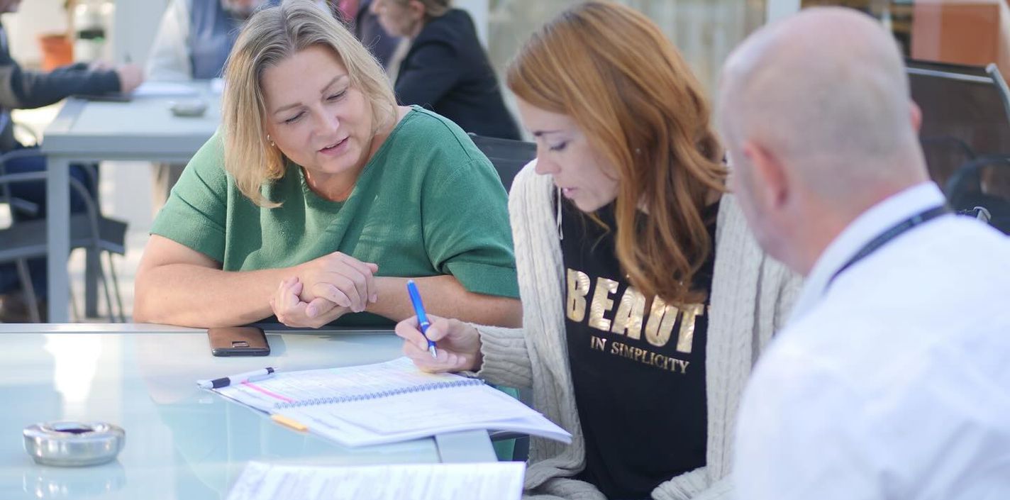 Tři účastníci výcviku sedí spolu nad zápisky a probírají zadání